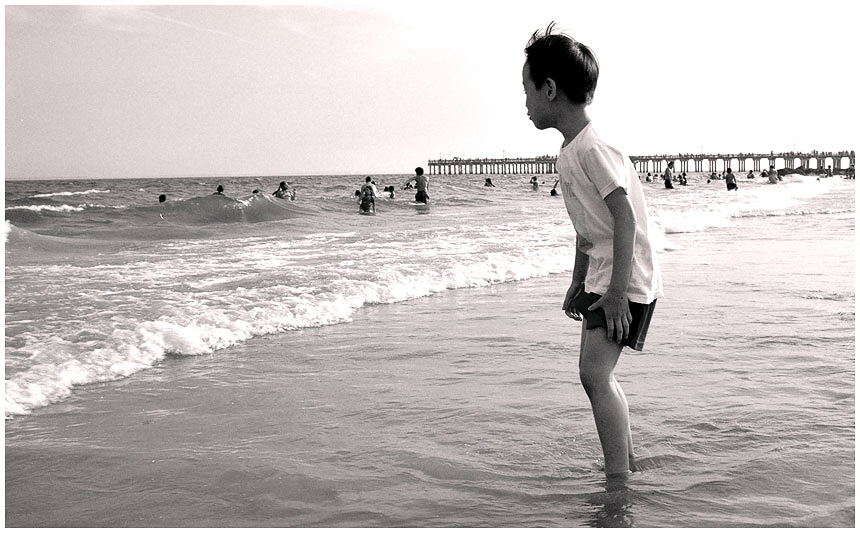 a boy standing on a beach holding a ball