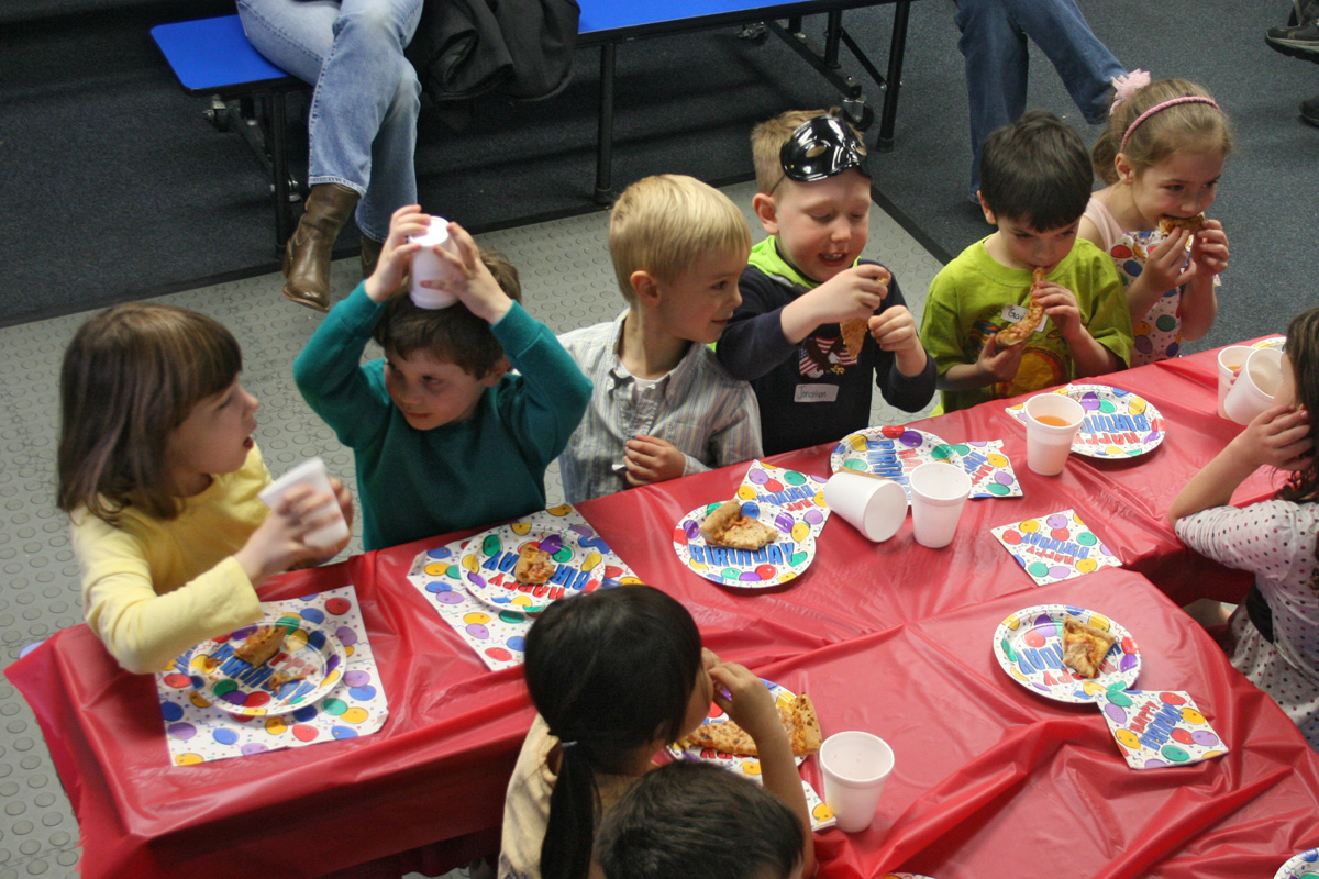 young children are eating at red tables in a classroom