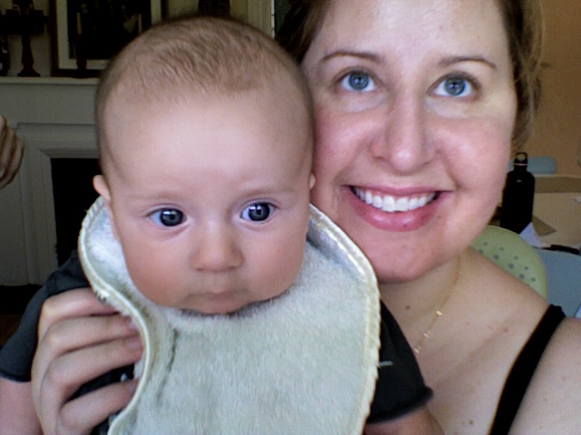 a woman holds up her baby who is wearing a bib
