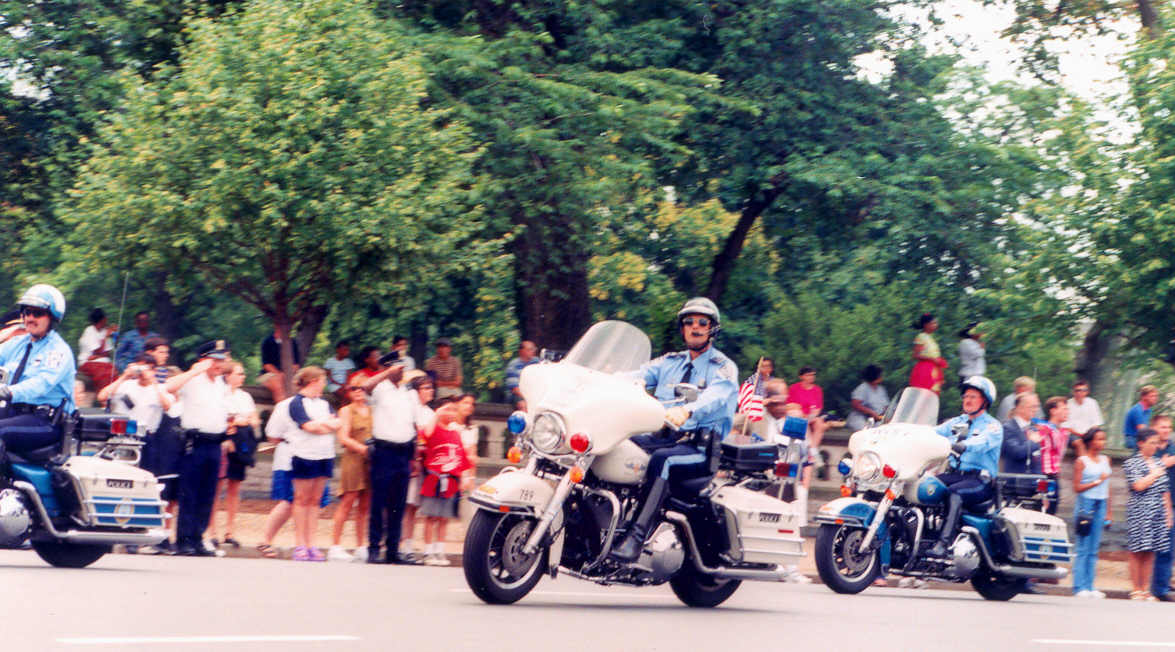 people watching two police officers on motorcycles driving down the road