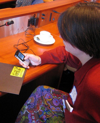 a woman holding up a smart phone at a desk with a box
