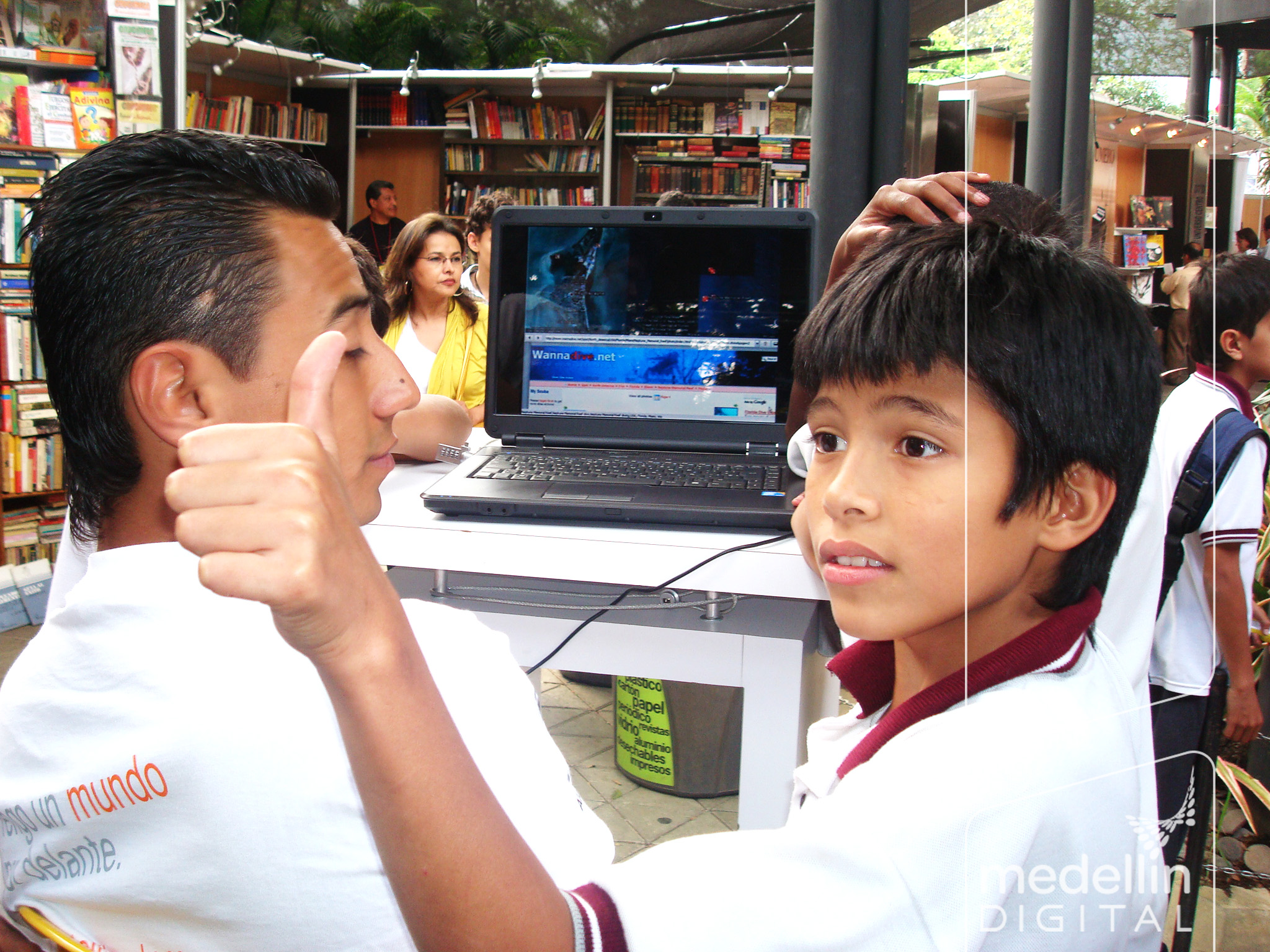 a boy on a laptop being examined by an adult in a public liry
