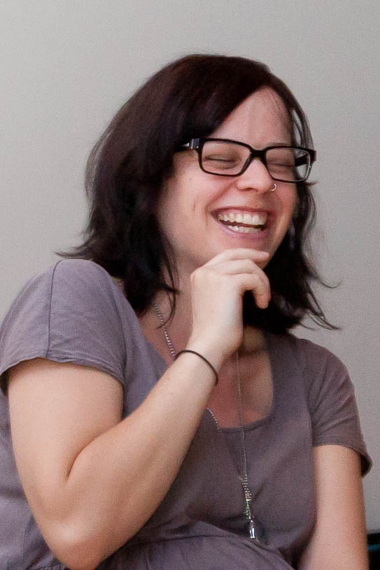 a woman in glasses smiles and holds up a wii controller