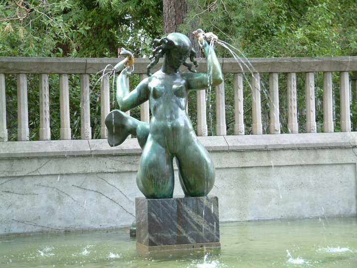 a statue of a  woman holding fish next to a park