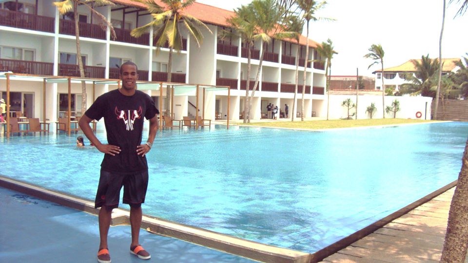 a man wearing a black t - shirt standing in front of a large pool with a el in the background
