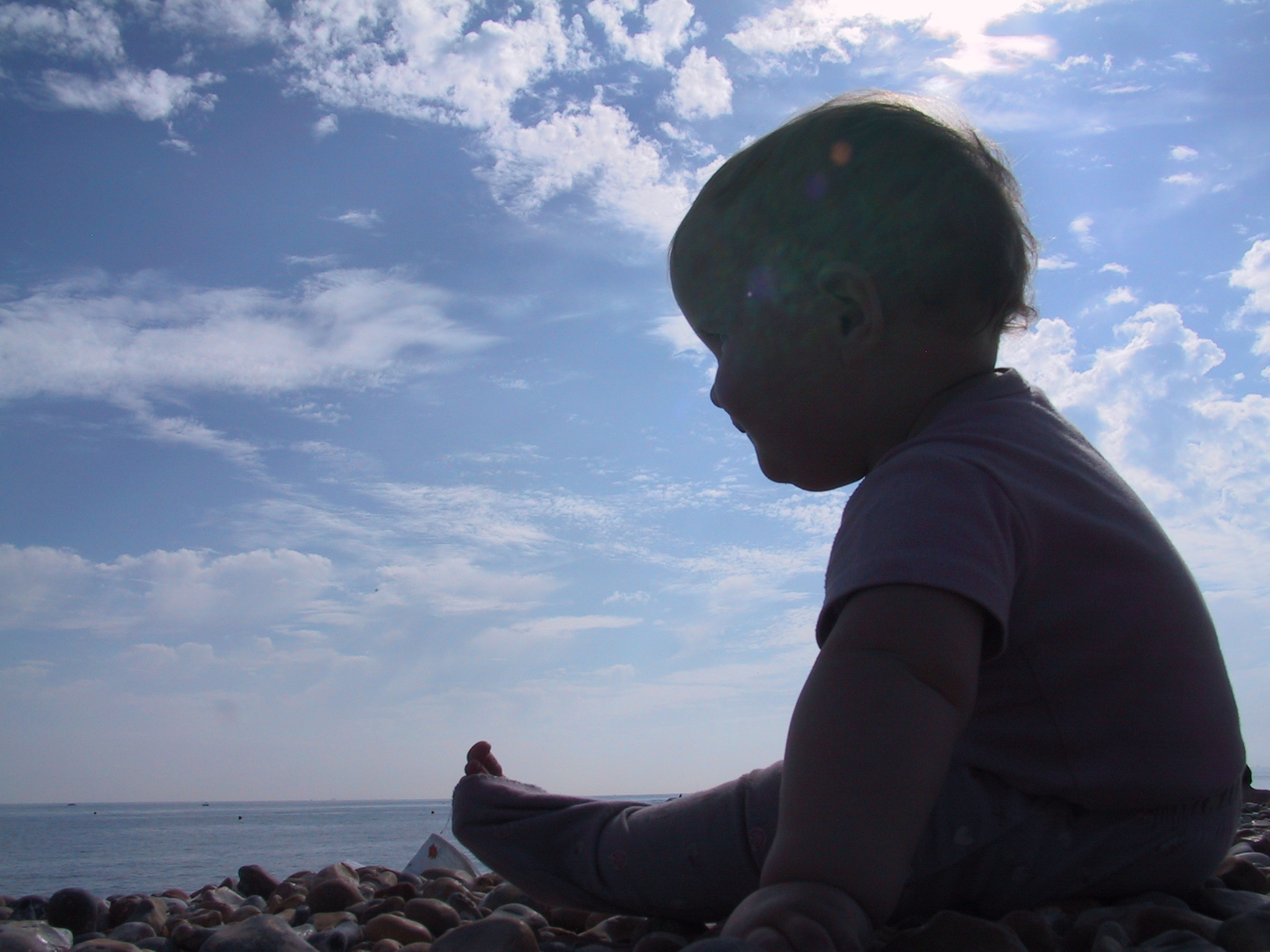 a young child sitting on a beach looking at the water