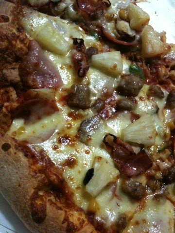 a thin crust pizza with sausage, pineapple, and onion slices
