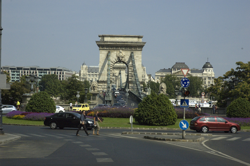 several cars in the road at the intersection of a street with tall buildings