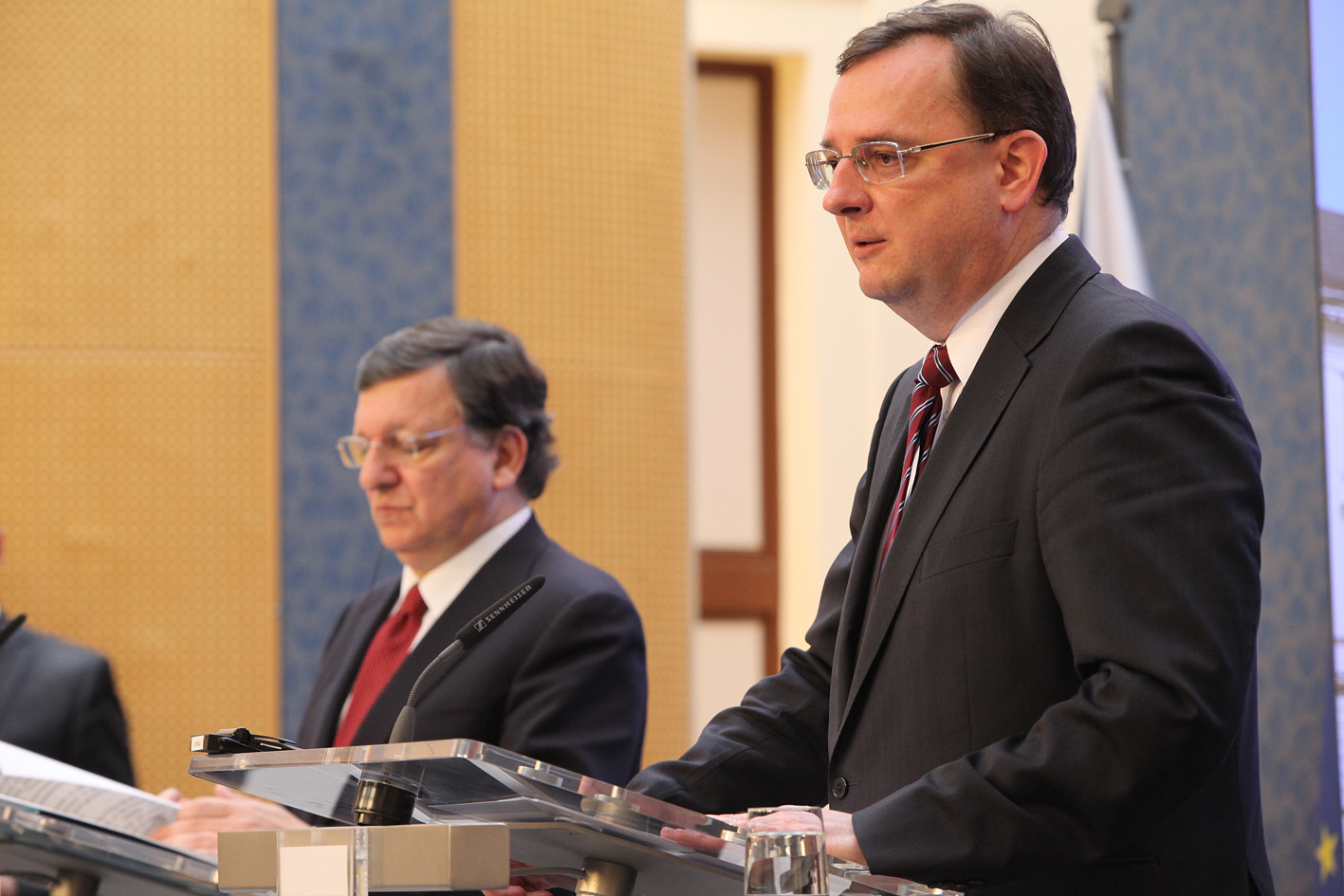 two men wearing business suits stand at a podium