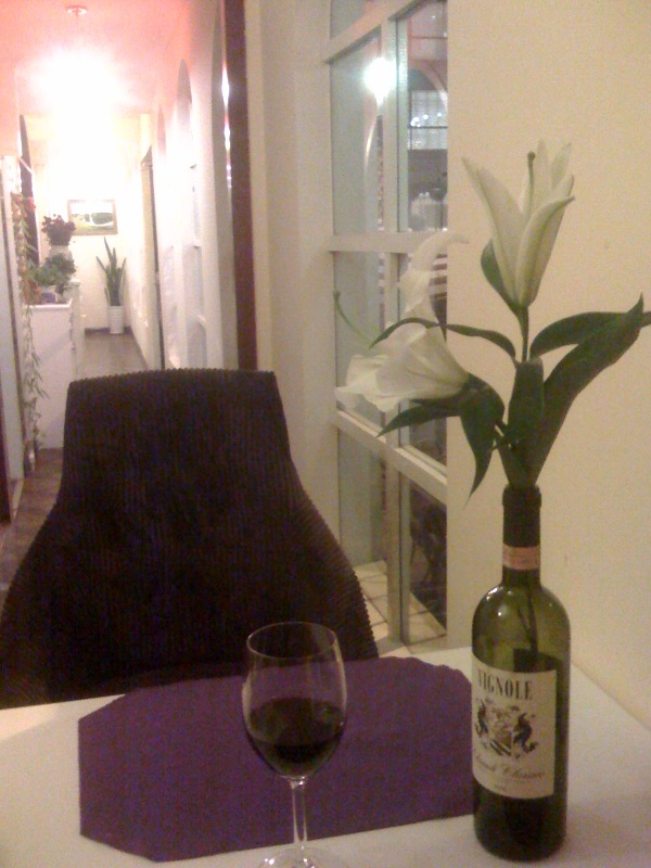 an empty wine glass, a bottle, and a plant sit on a white table