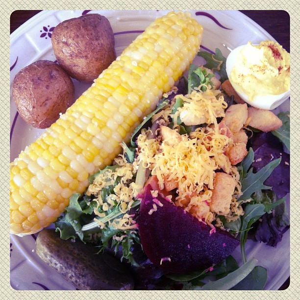 a close up of a plate with vegetables and corn on the cob