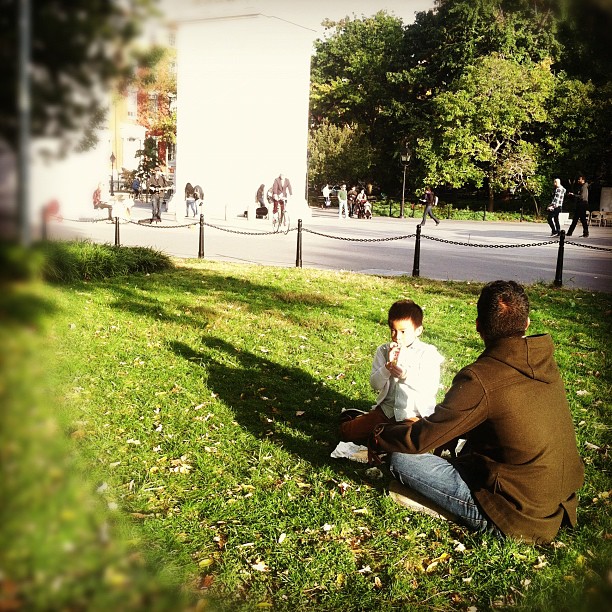 a man sitting on the ground while next to a boy on a phone