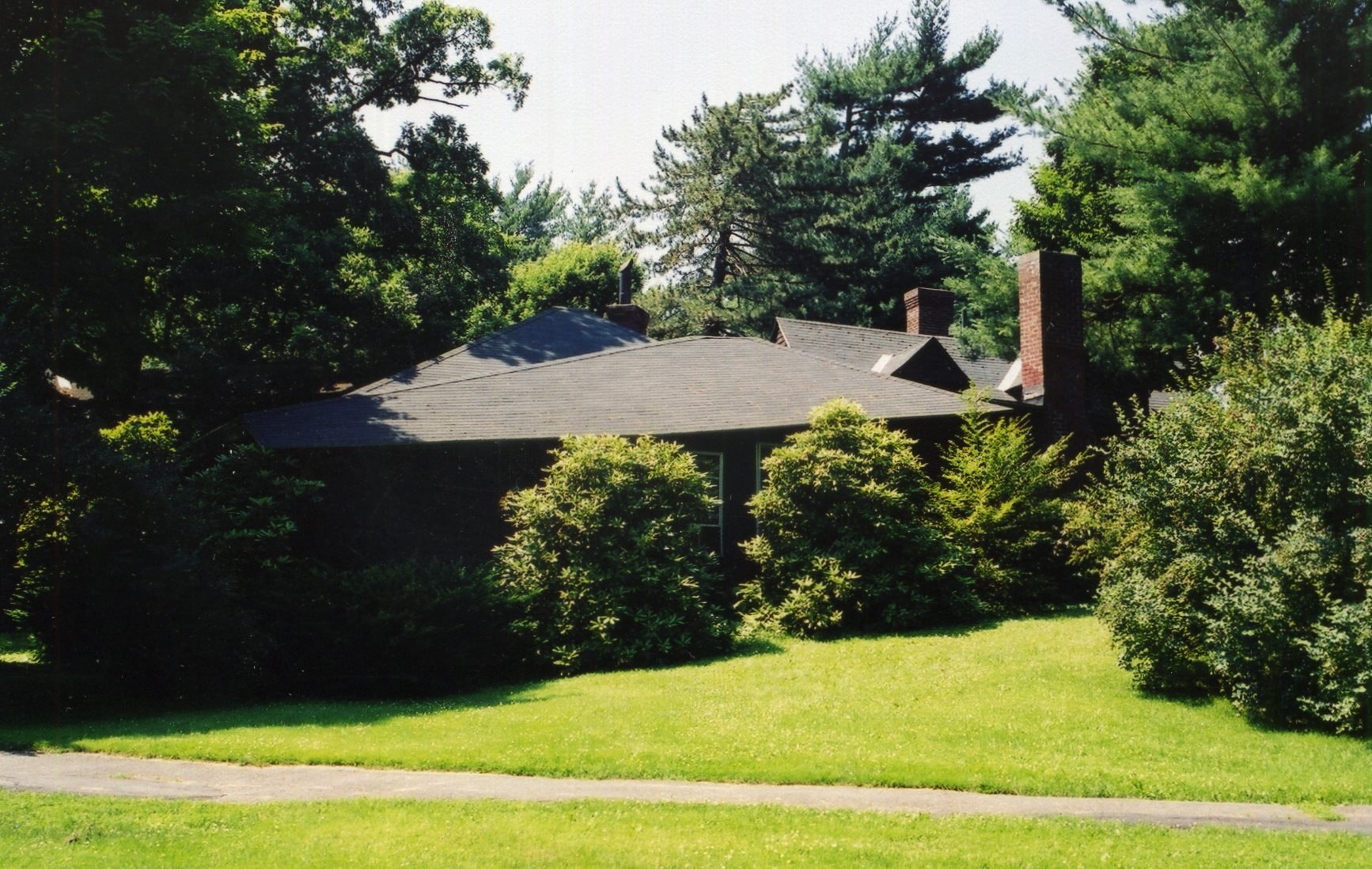 there is a black house that is standing among green grass and trees