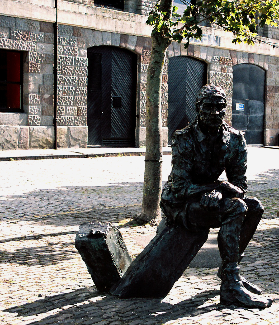 a bronze statue sitting on the ground near a tree
