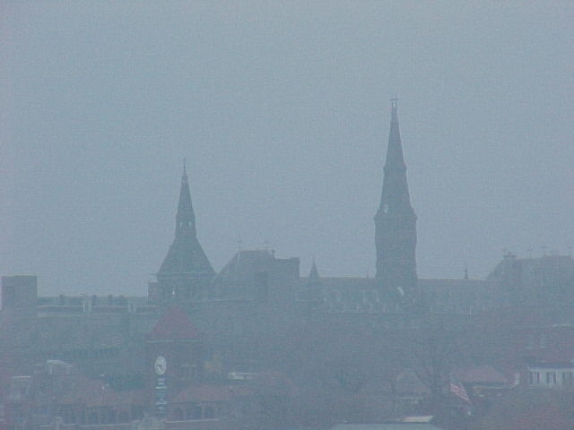 fog over skyline of buildings with spires and clock in the distance