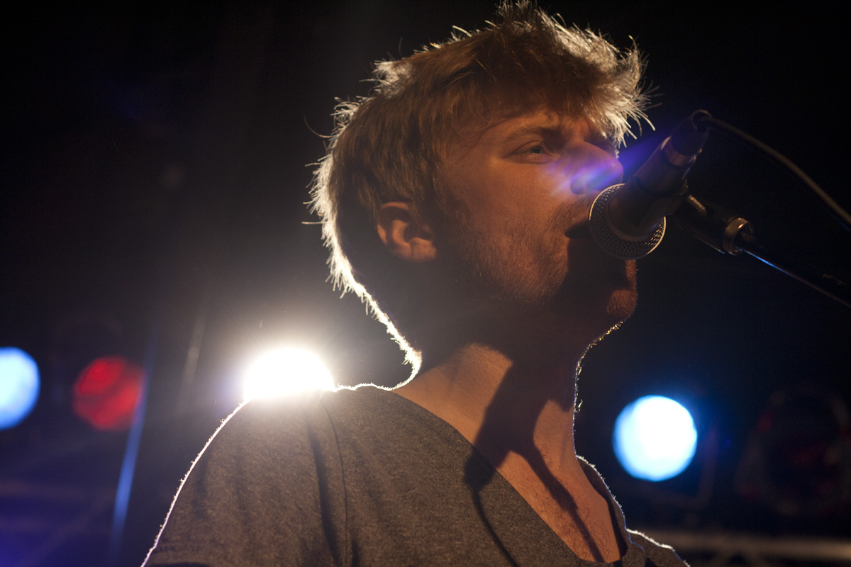 a man in a microphone singing in front of a dark stage