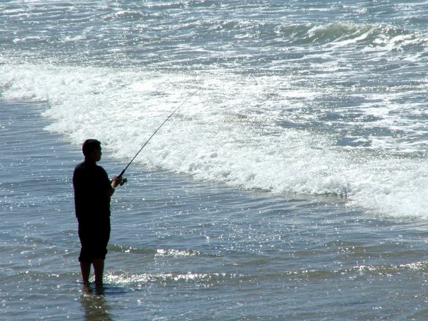 a man fishing in the ocean from the beach