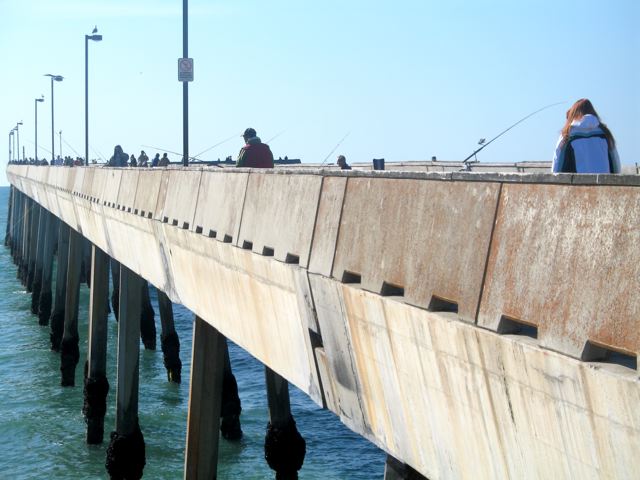 people are fishing at the edge of a wooden pier