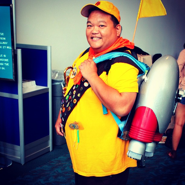 a person in a yellow shirt and black and white backpack with an umbrella and a cup in his hands