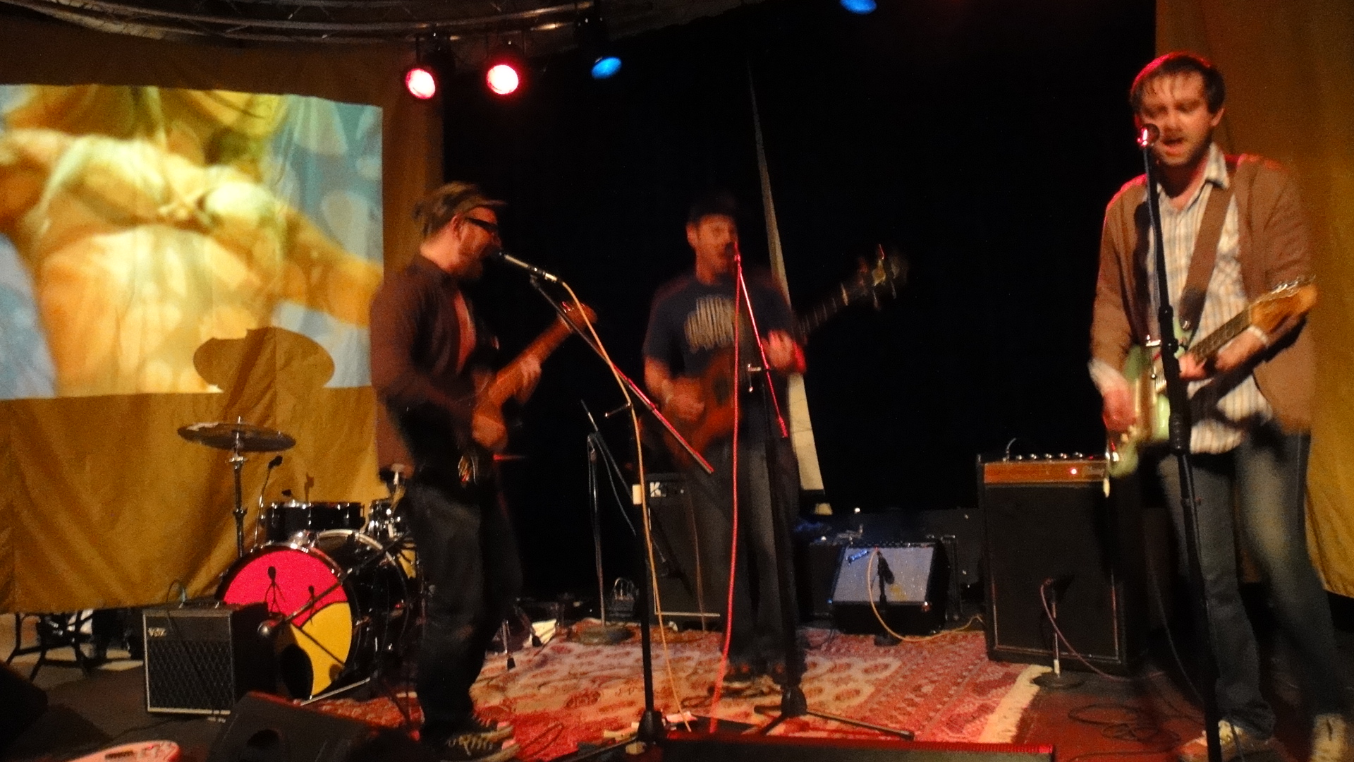 three men on a stage one playing guitar and the other singing on a bass