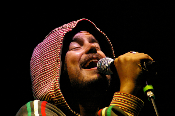 man with colorful scarf singing into microphone on stage