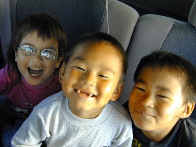 three children sitting in a vehicle seat with one child in the back