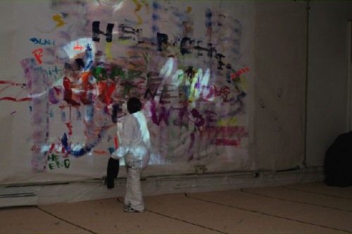the little boy is standing near a wall covered in graffiti