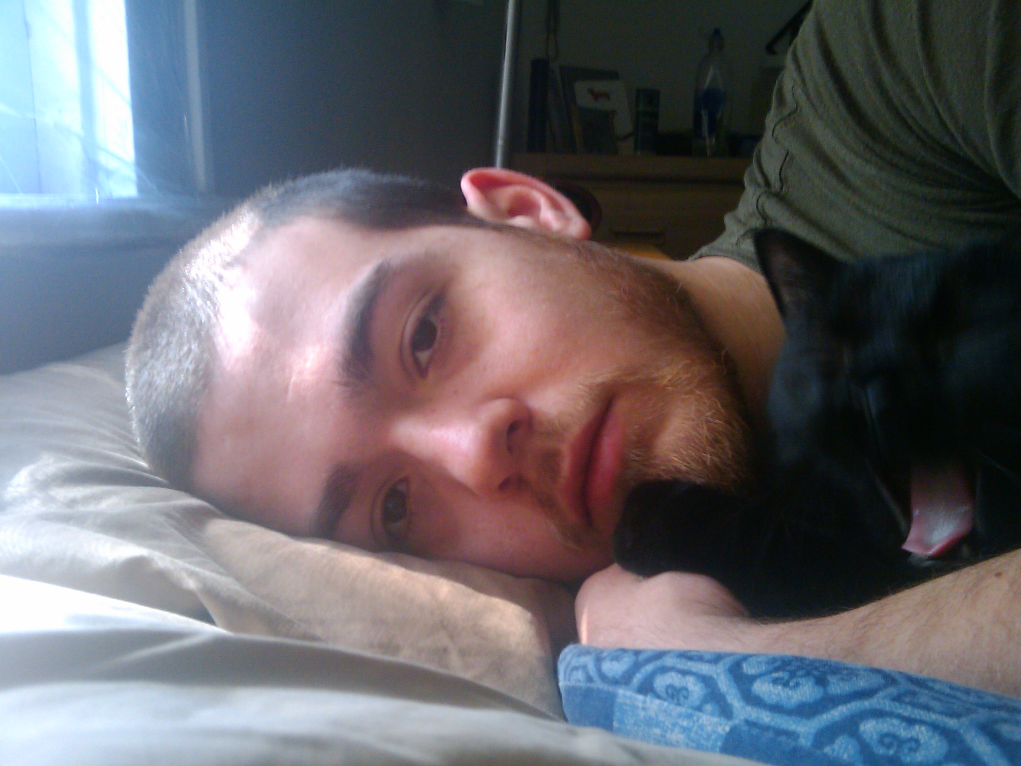 a man lays down with his cat on his bed