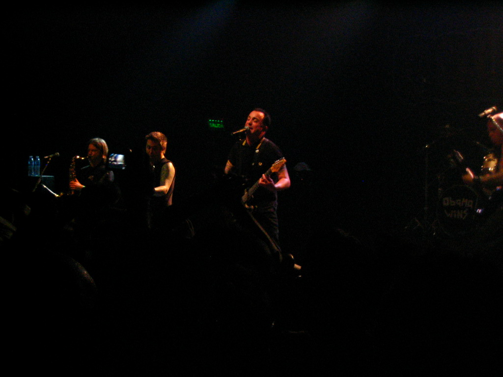 four people are standing on stage singing in front of a microphone