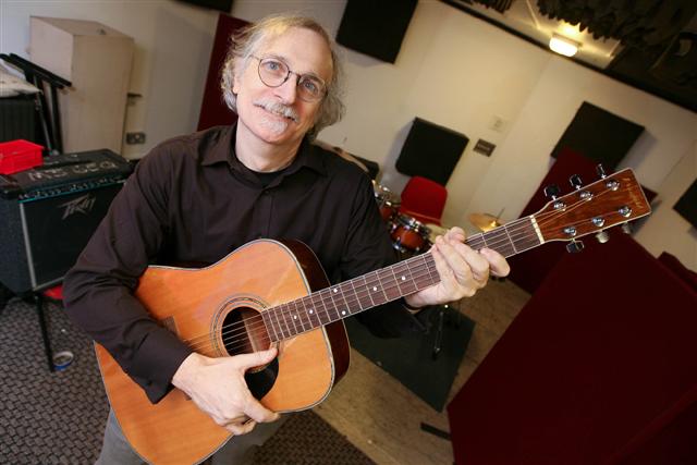a man wearing glasses is holding an acoustic guitar