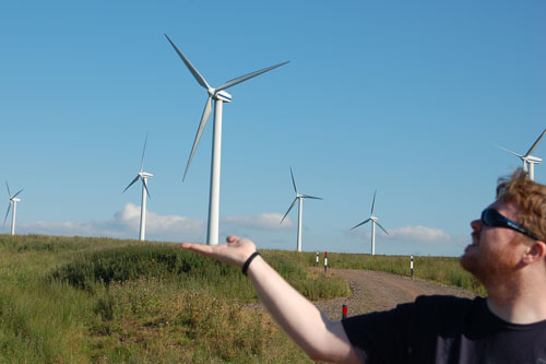 a man on a road pointing to wind turbines