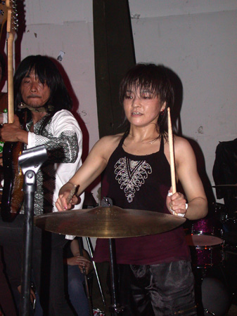 a woman playing drums while another man sits on the floor