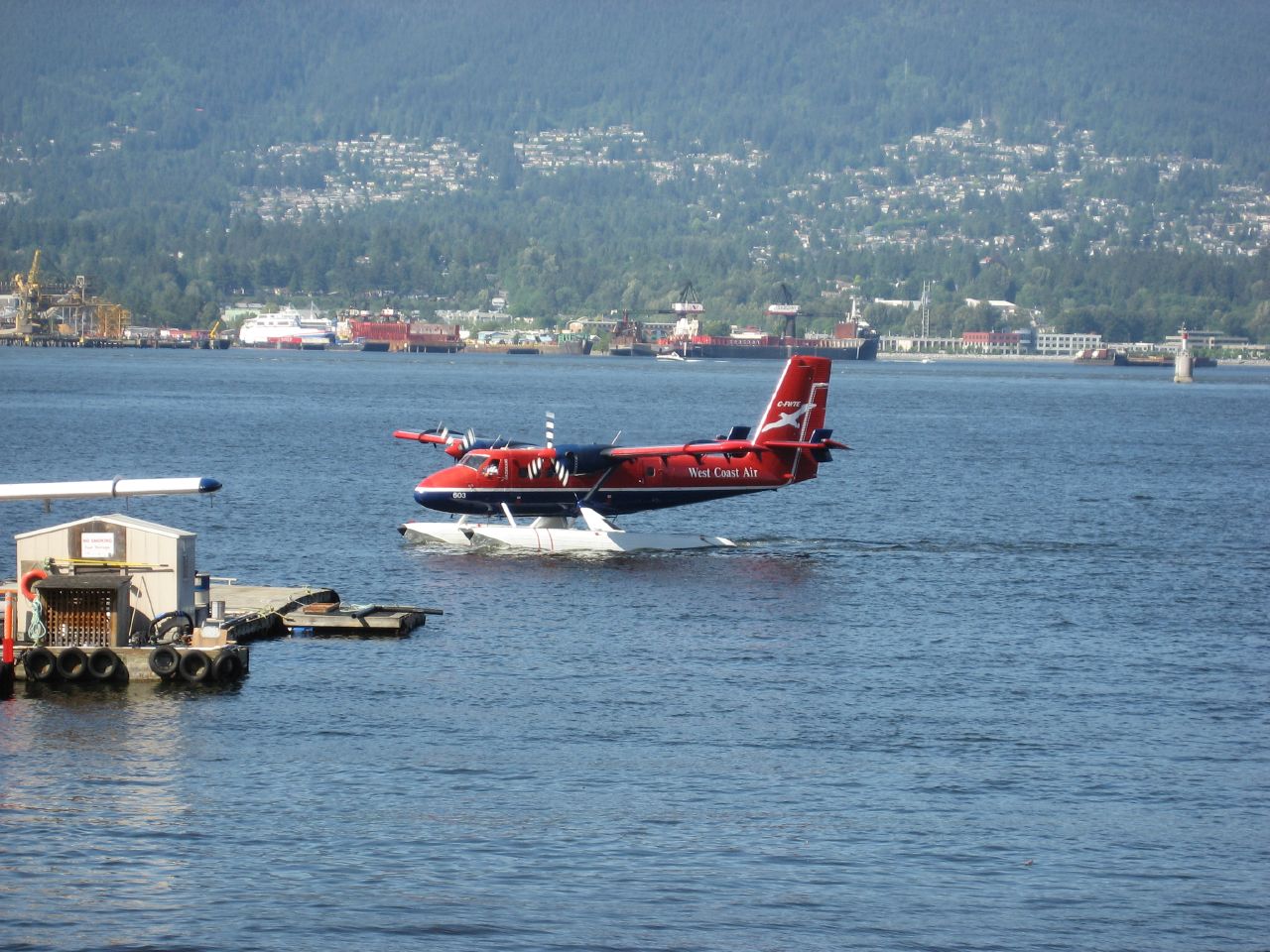 a red and white plane flying over water next to a boat
