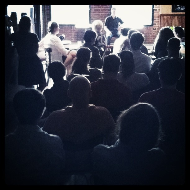 people sitting in chairs at a conference, with one woman presenting