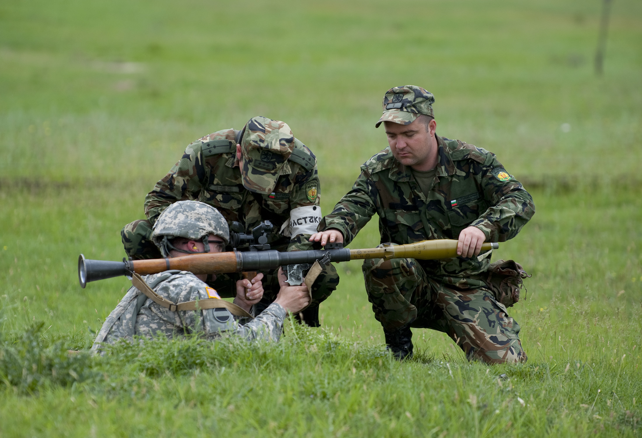 two army men crouch over a man aiming a rifle