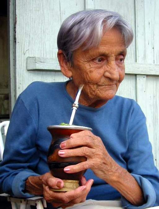 an old woman drinks tea on a white table outside a barn