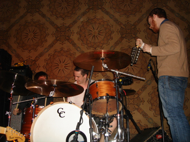 two guys playing instruments in front of a wallpaper