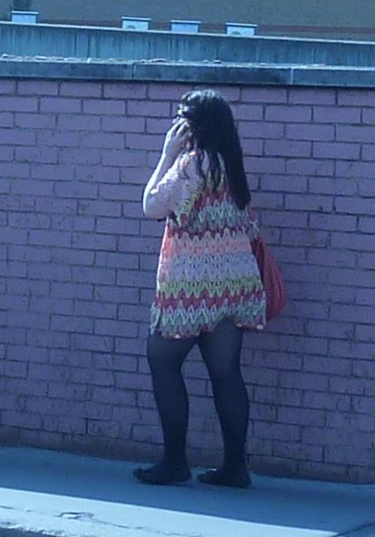 a woman standing next to a brick wall talking on a cell phone