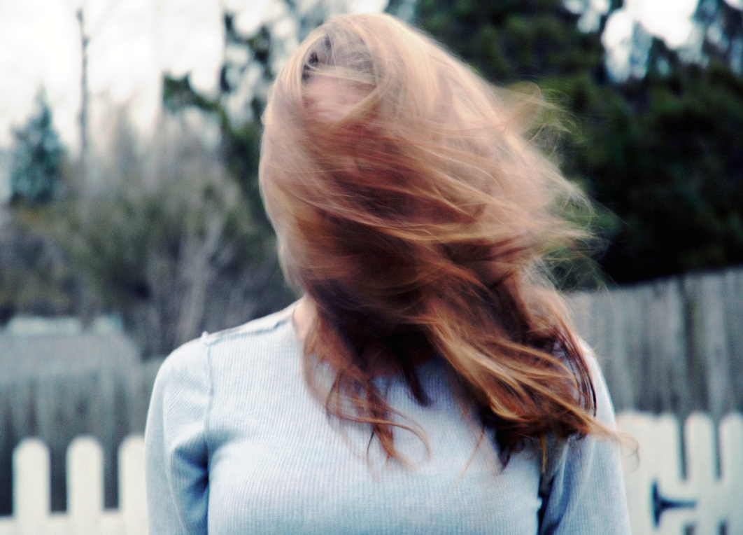 long haired woman standing outside next to fence