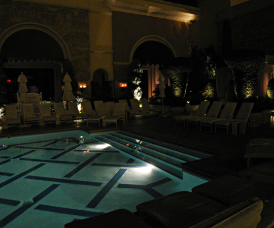 chairs and tables are around the edge of a pool at night
