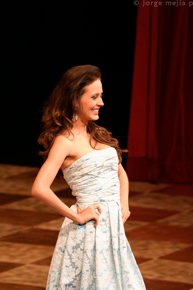 a smiling woman in a blue dress with her hands on her hips