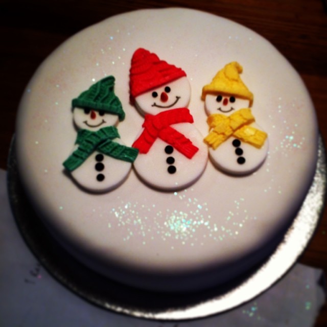 the decorated cake has three small snowmen wearing colorful hats