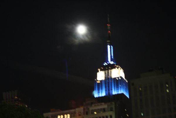 a full moon and the top of empire building lit up