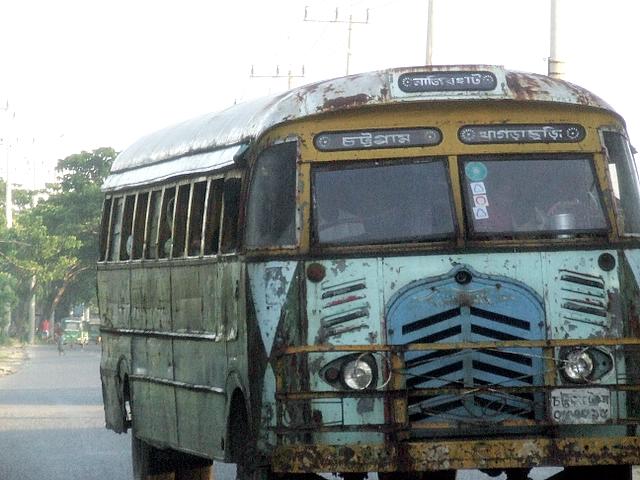old rusty bus drives down the road with it's door open