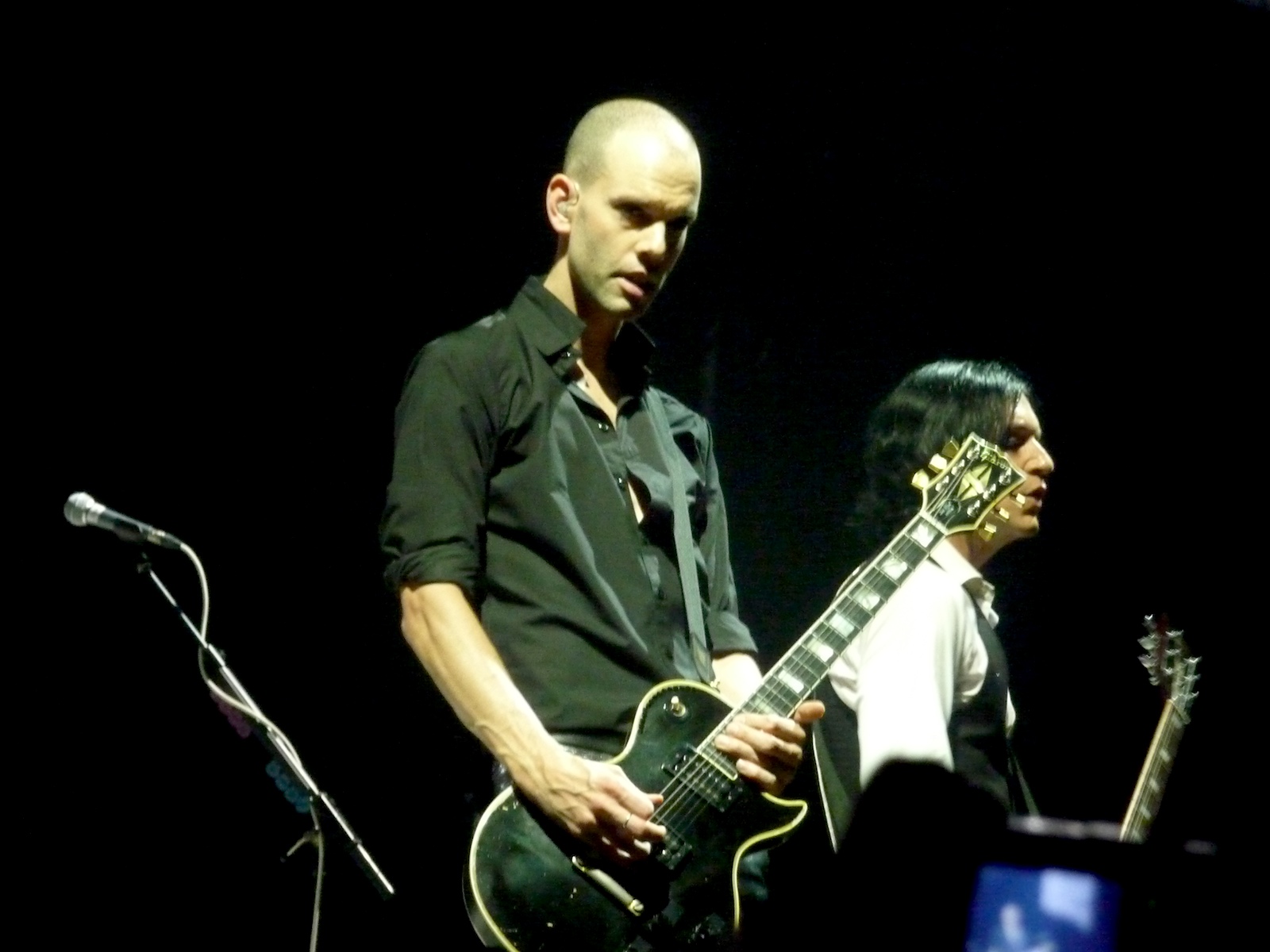 a man playing guitar on stage while another man plays a guitar