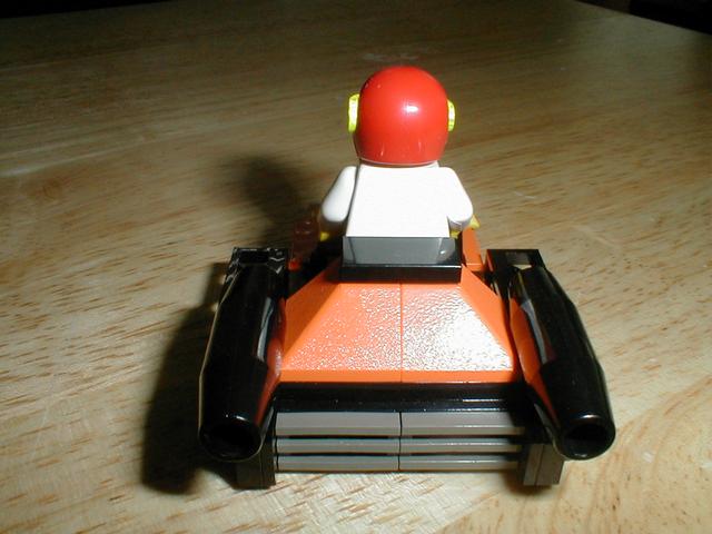 a lego figure riding an orange car on a wooden table
