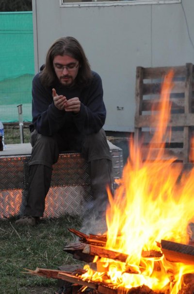 man sitting next to campfire, looking at cell phone