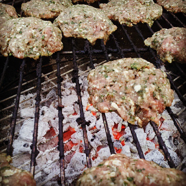 a hamburger on a grill with other hamburgers cooking