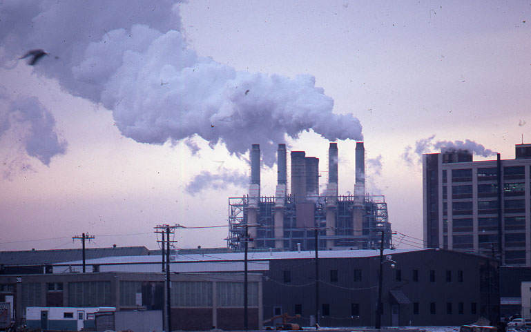 smoke rises from chimneys behind a factory as the sun sets