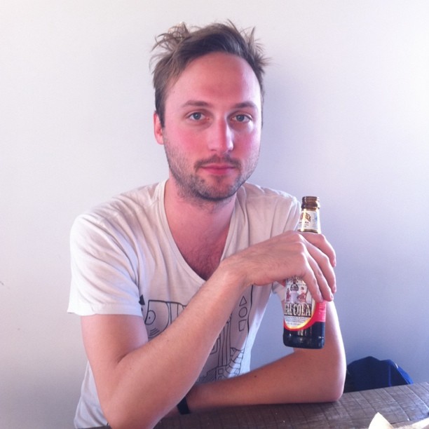 man sitting down at a table with his hand holding onto a beer